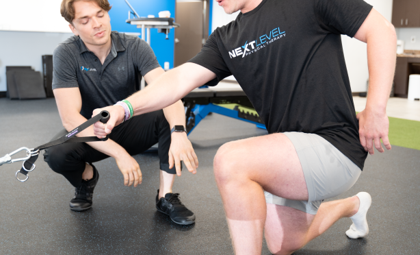 Physical therapist helping a patient with his form as she performs a cable pull back at Next Level Physical Therapy in Marlton, NJ