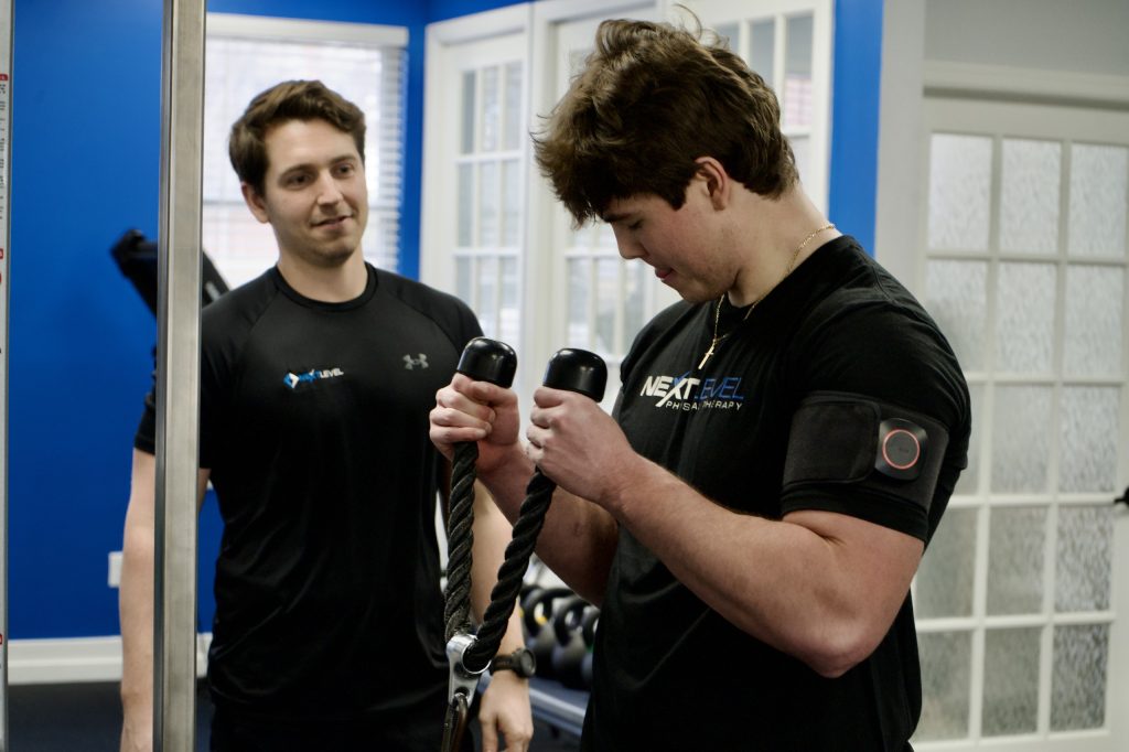 Physical therapist overseeing patient performing cable bicep curls at Next Level Physical Therapy in Hamilton, NJ