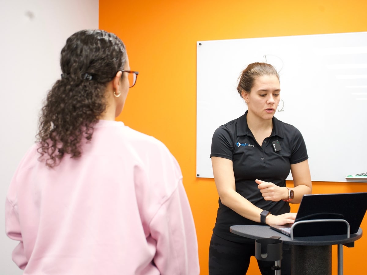 A physical therapist reviews running gait analysis data on a laptop with a patient in a clinic, discussing results in front of a whiteboard.